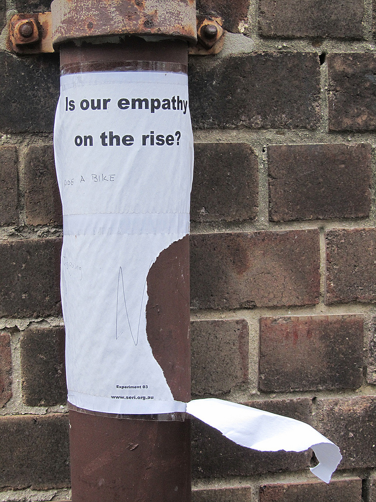poster with question, "Is our empathy on the rise?" halfway torn from rusty pipe where it was posted.