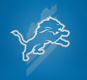 An image of the logo of the Detroit Lions, a simple blue side profile of a lion outlined in white. It lunges towards the right. Behind it is a faded image of some Detroit buildings and three wide, diagonal stripes.